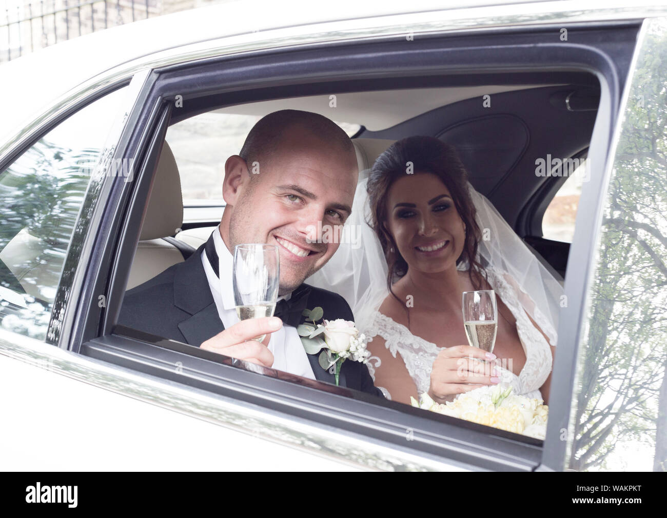 a newly wed couple toasting champagne from a Bentley wedding car Stock Photo