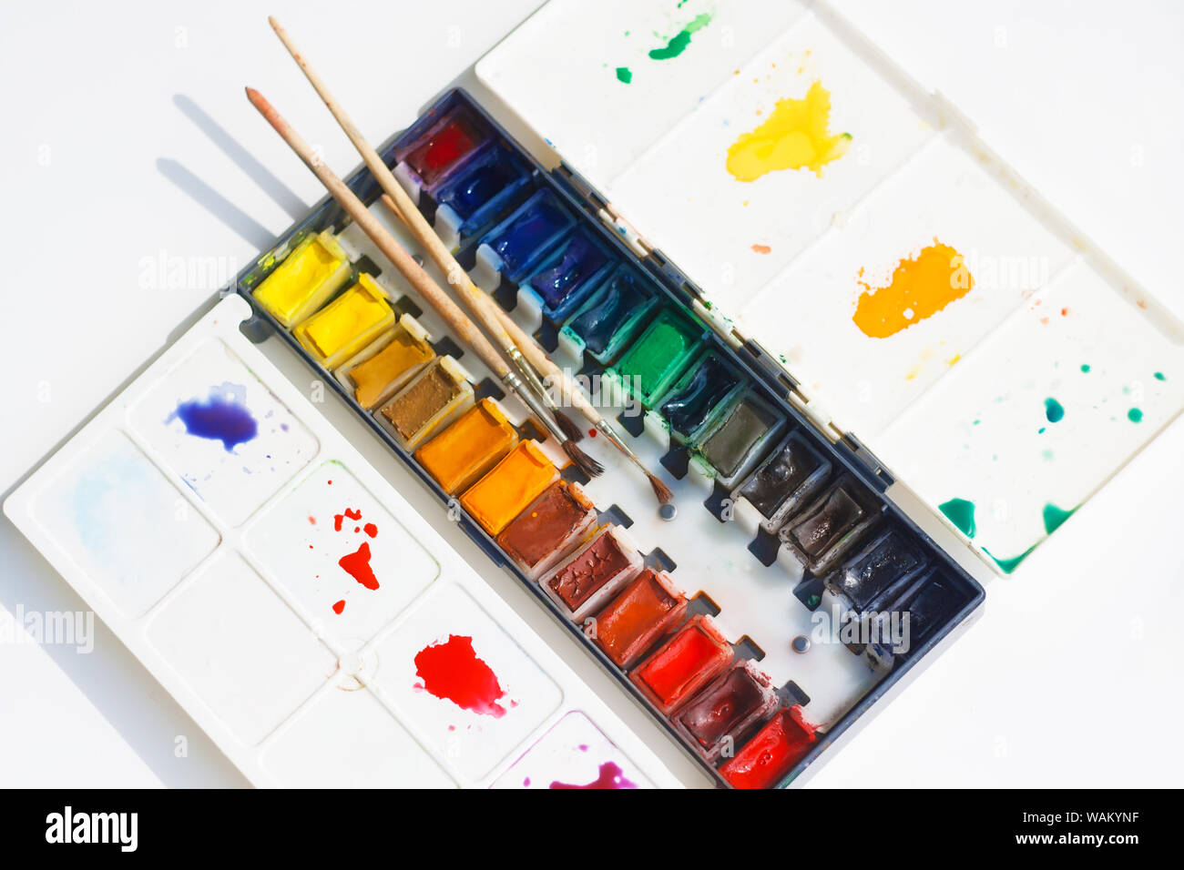 Watercolor paints with a lot of shades are in a plastic box with a palette on which stains of different colors, as well as in the set are three brushe Stock Photo