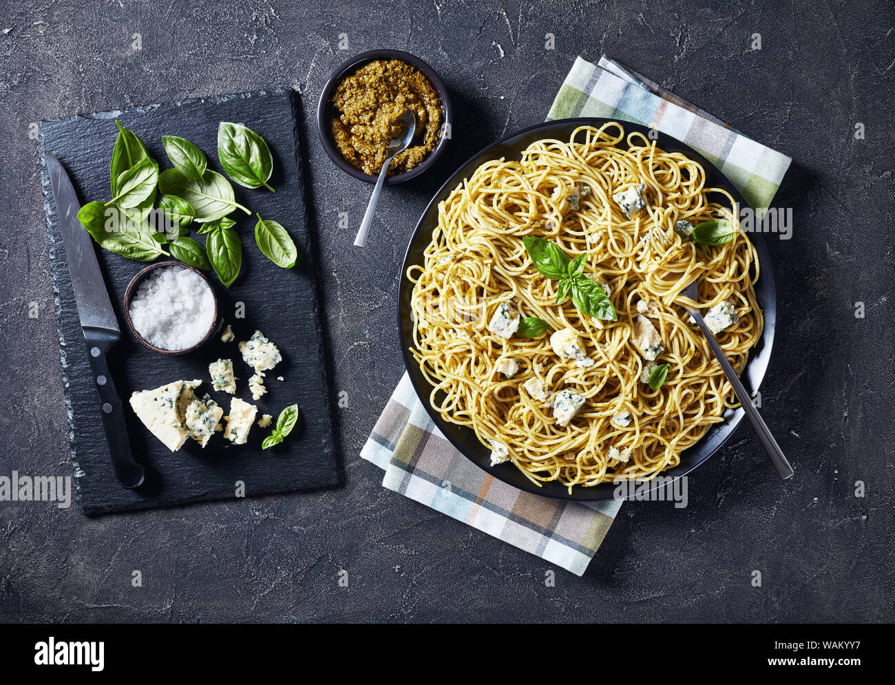 Spaghetti with genovese basil pesto and blue cheese on a black plate on a concrete table with