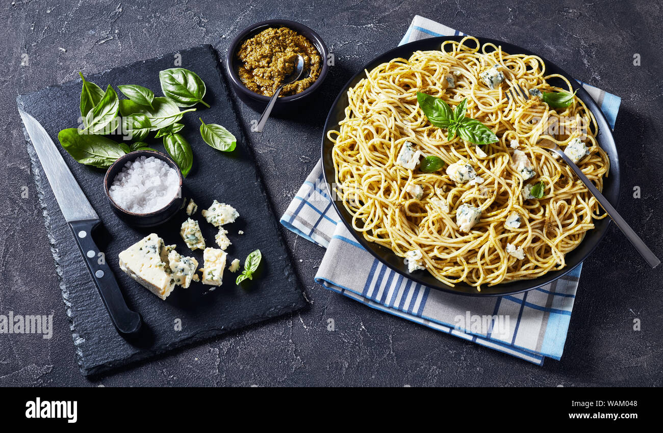close-up of delicious Spaghetti with basil pesto and blue cheese on a black plate on a concrete table, Italian cuisine, horizontal view from above Stock Photo