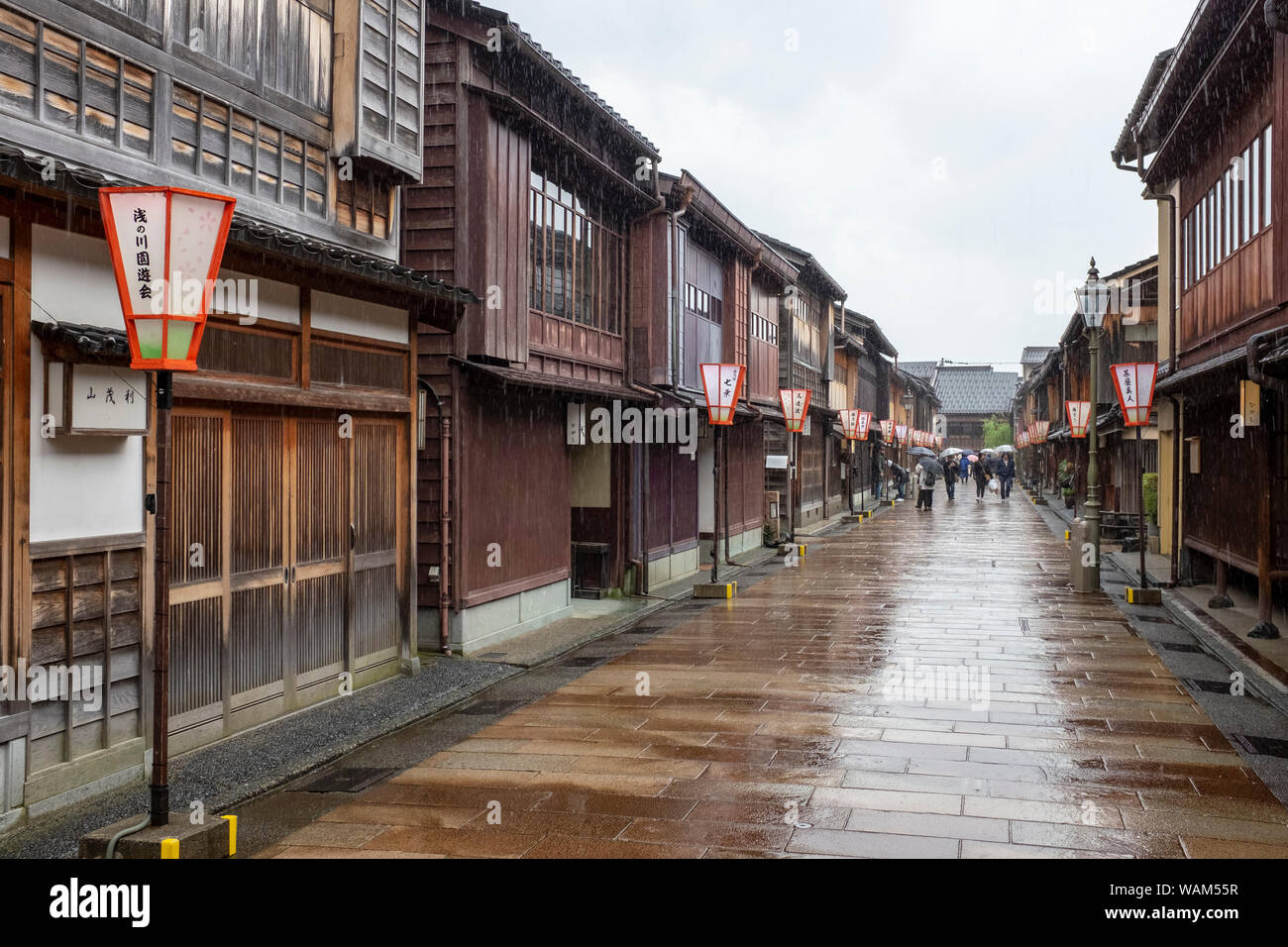 Tourists walking with umbrellas in the rain past traditional teahouses and buildings in the Higashi Chaya geisha district, Kanazawa, Japan Stock Photo