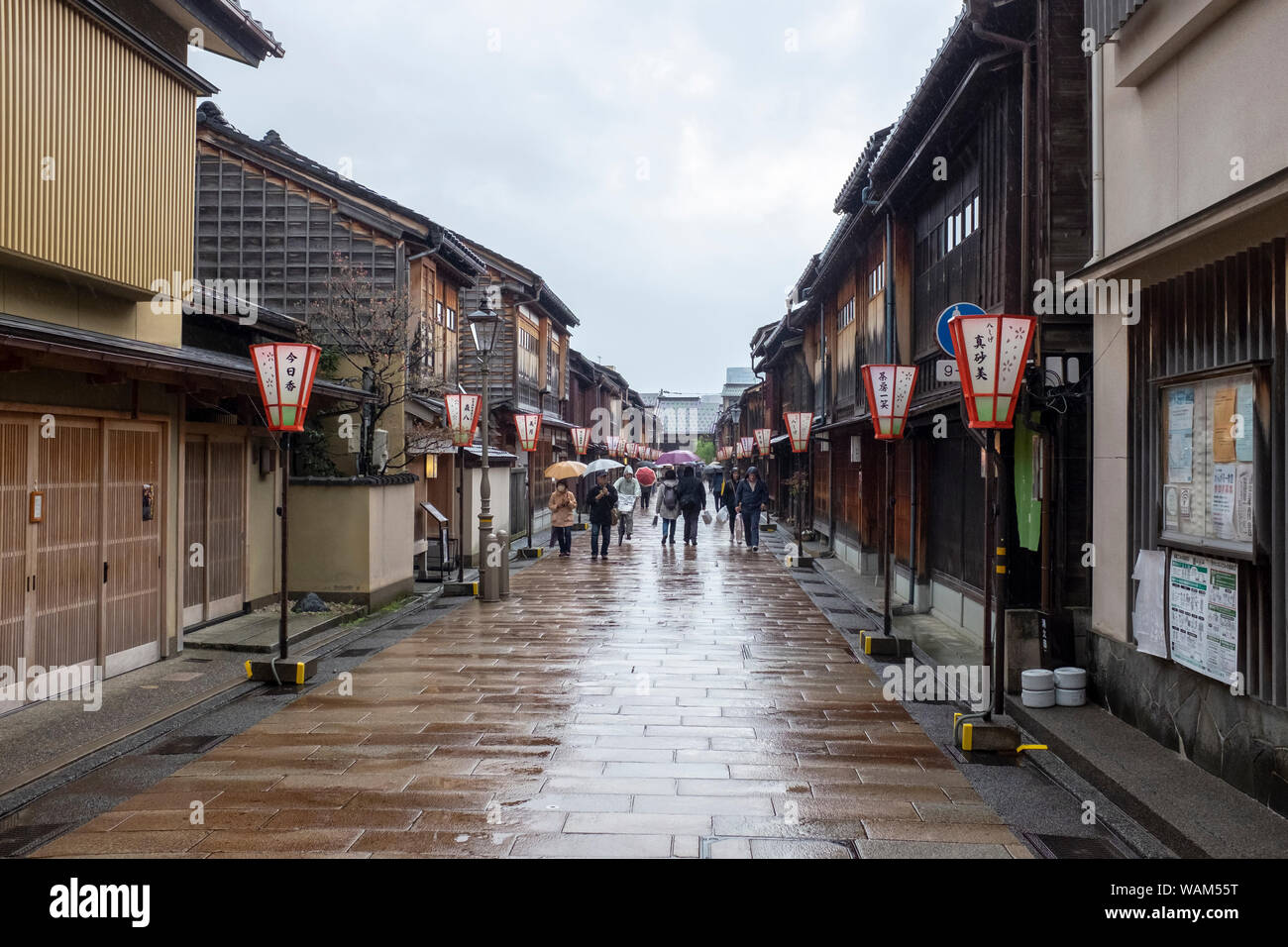 Tourists walking with umbrellas in the rain past traditional teahouses and buildings in the Higashi Chaya geisha district, Kanazawa, Japan Stock Photo