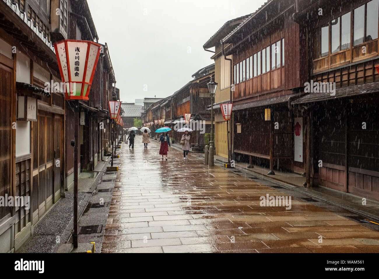Tourists walking with umbrellas in the rain past traditional teahouses and buildings in the Higashi Chaya geisha district, Kanazawa, Japan Stock Photo