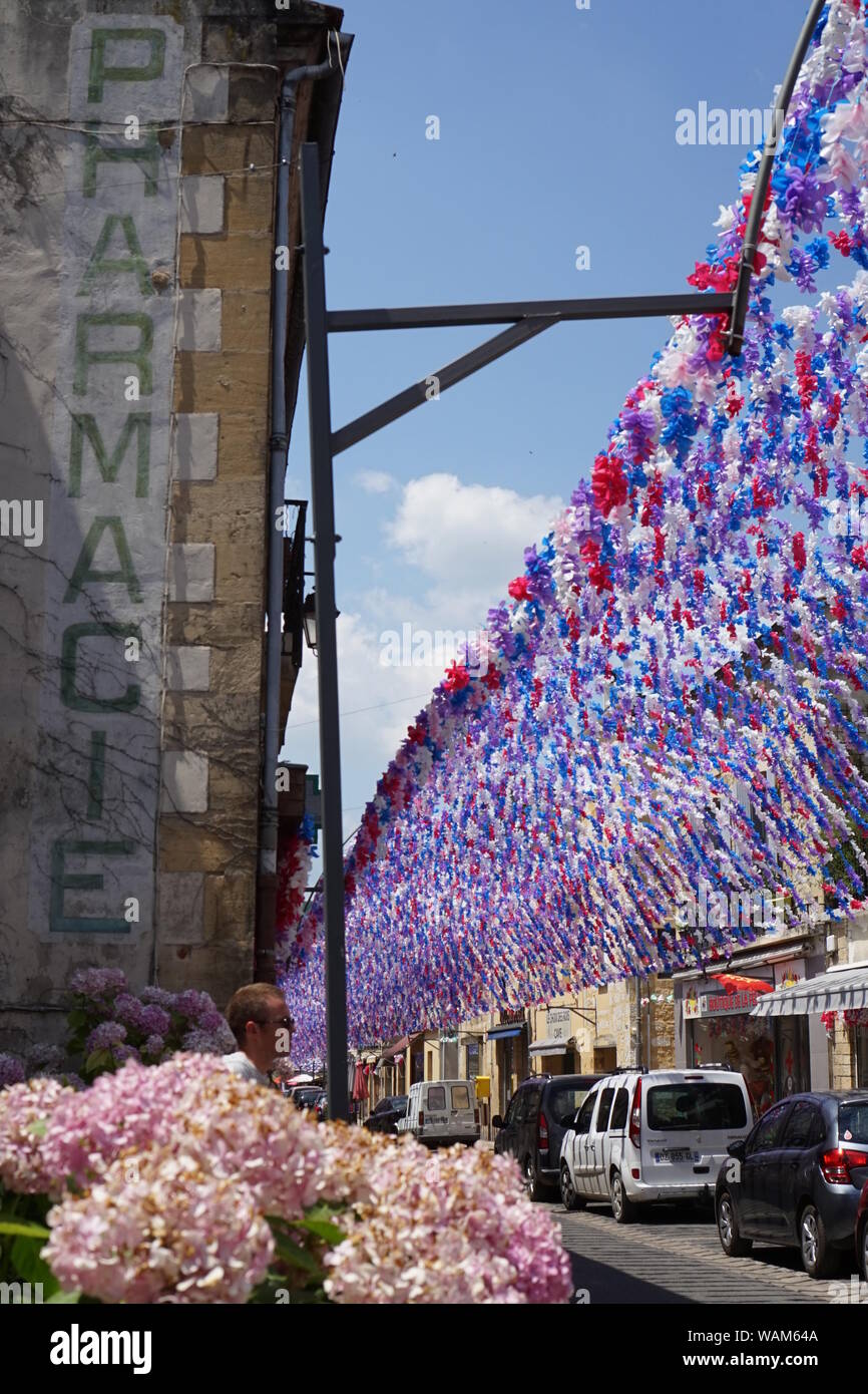 Street scene decorated with flower festival garlands with an old Pharmacie sign on the side of an old building Stock Photo