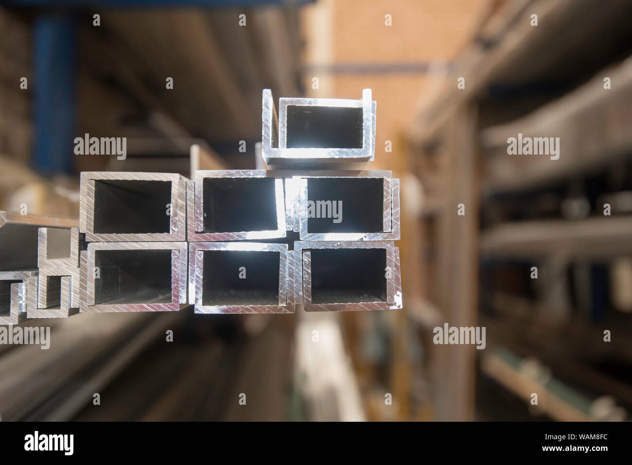 Milled lengths of Aluminium alloy extrusion profiles sitting on racking in a warehouse and lit with natural light Stock Photo