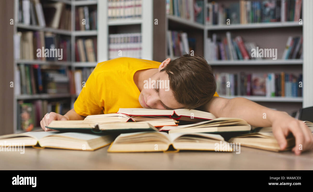 Tired guy napping on books in library Stock Photo
