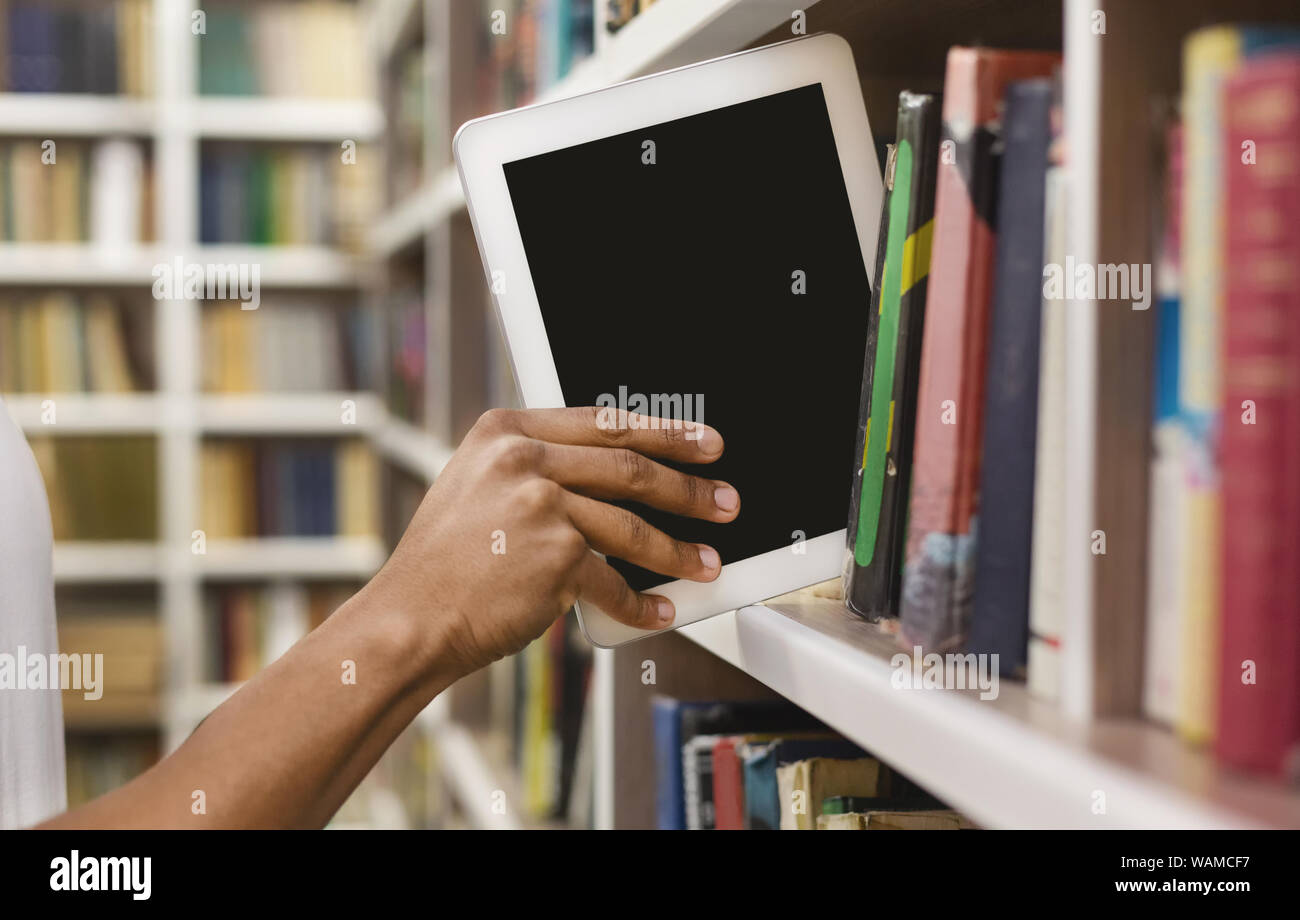 Afro student placing digital tablet on bookshelf Stock Photo
