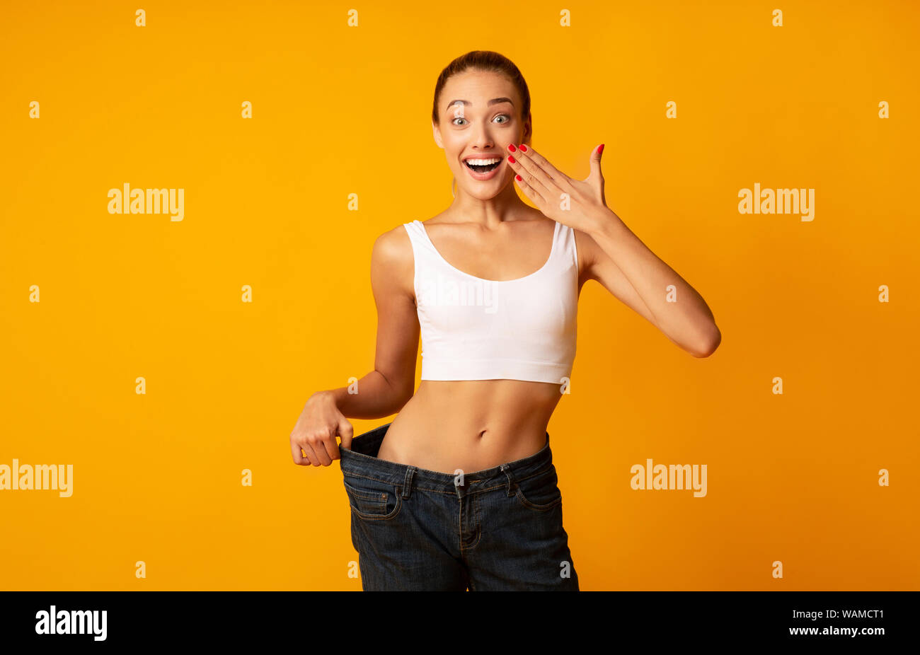 Excited Girl Posing In Oversize Jeans Over Yellow Studio Background Stock Photo