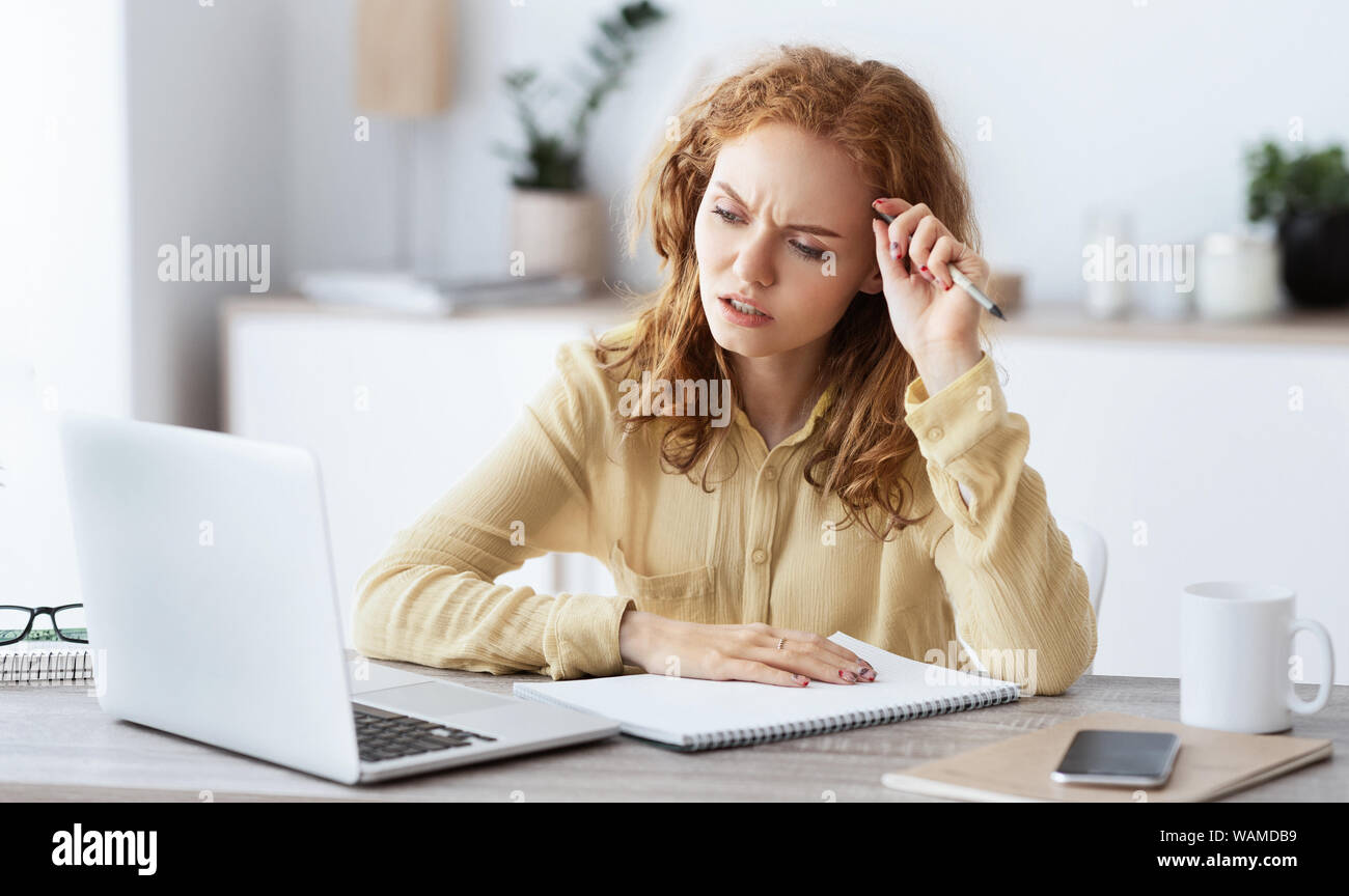 Bored woman with laptop and paperwork making notes Stock Photo