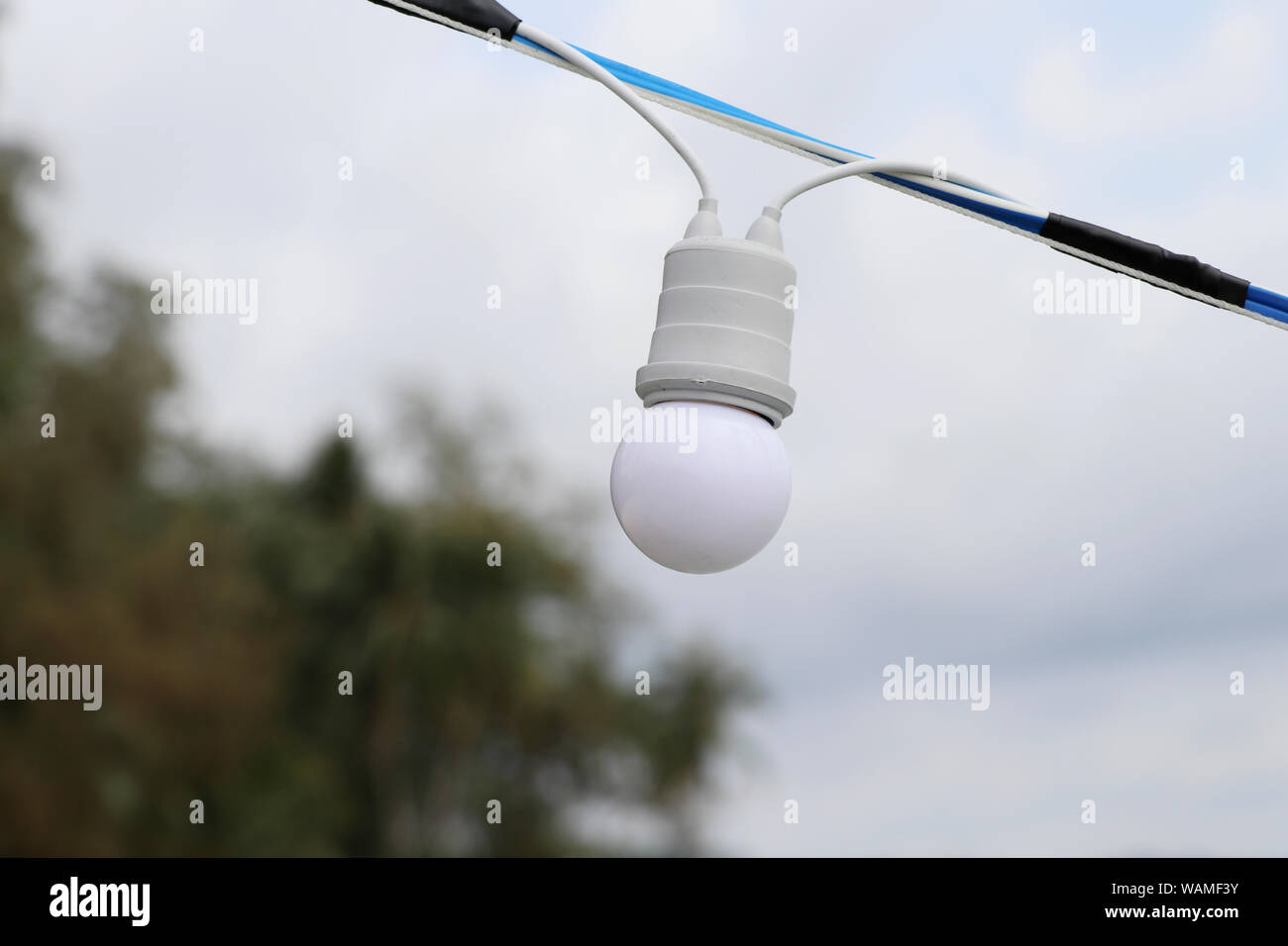 Round light bulb with a sky backdrop. White light bulb with blurred background. Stock Photo
