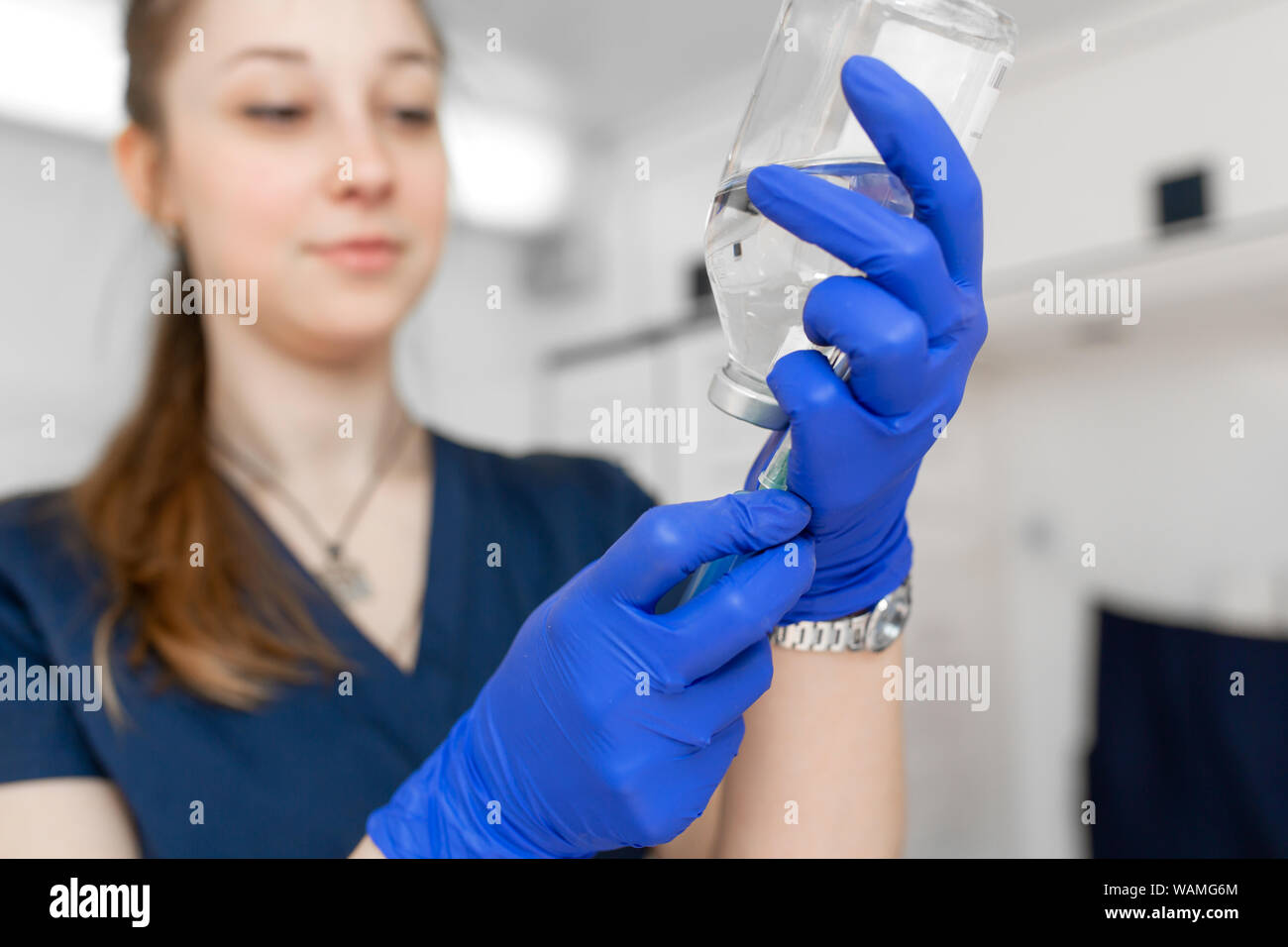 Young professional nurse in medical uniform, show syringe in her hands at ambulance background. Stock Photo