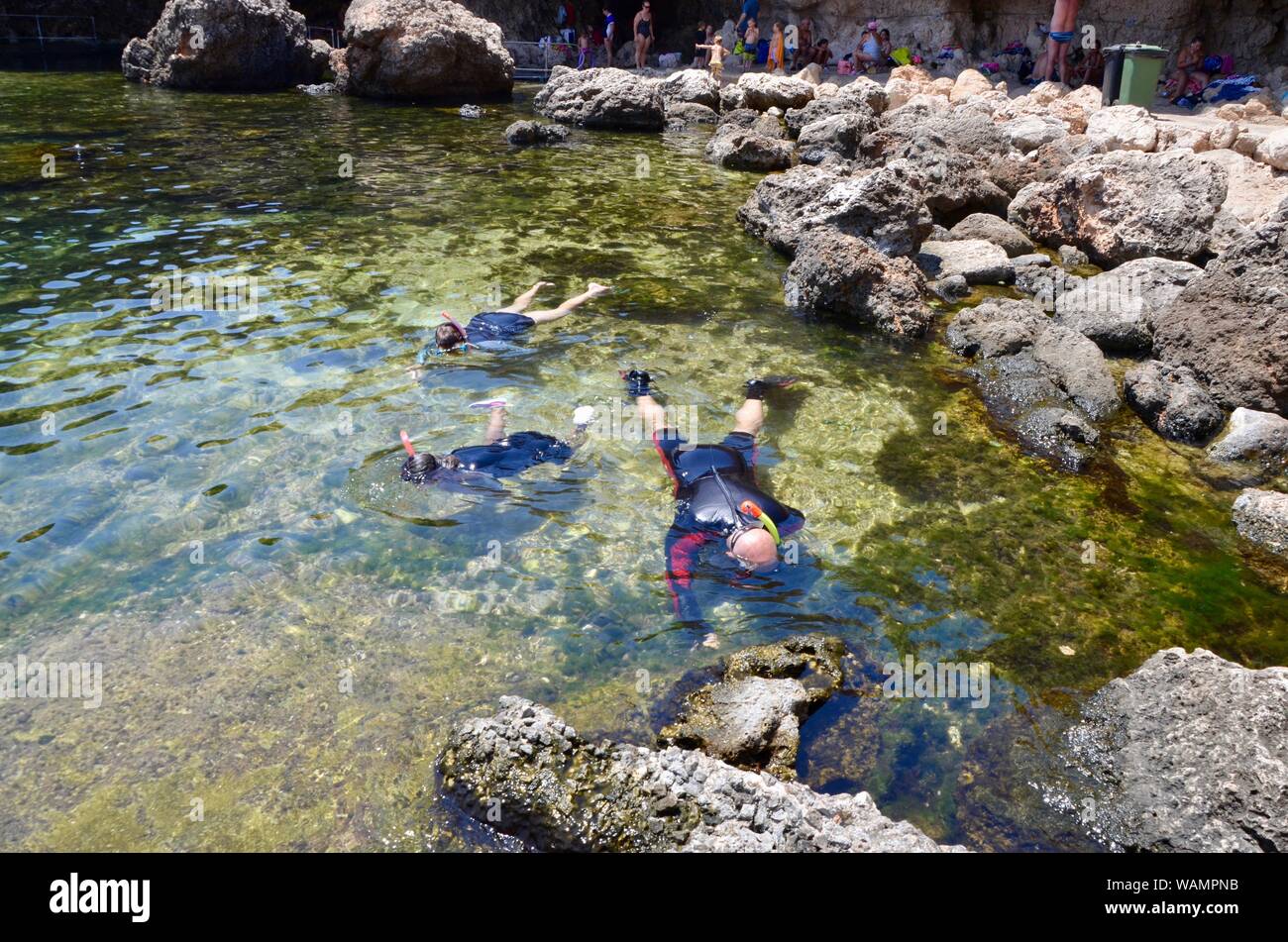 a family of snorkel wearing divers in wetsuits at Għar Lapsi Siġġiewi