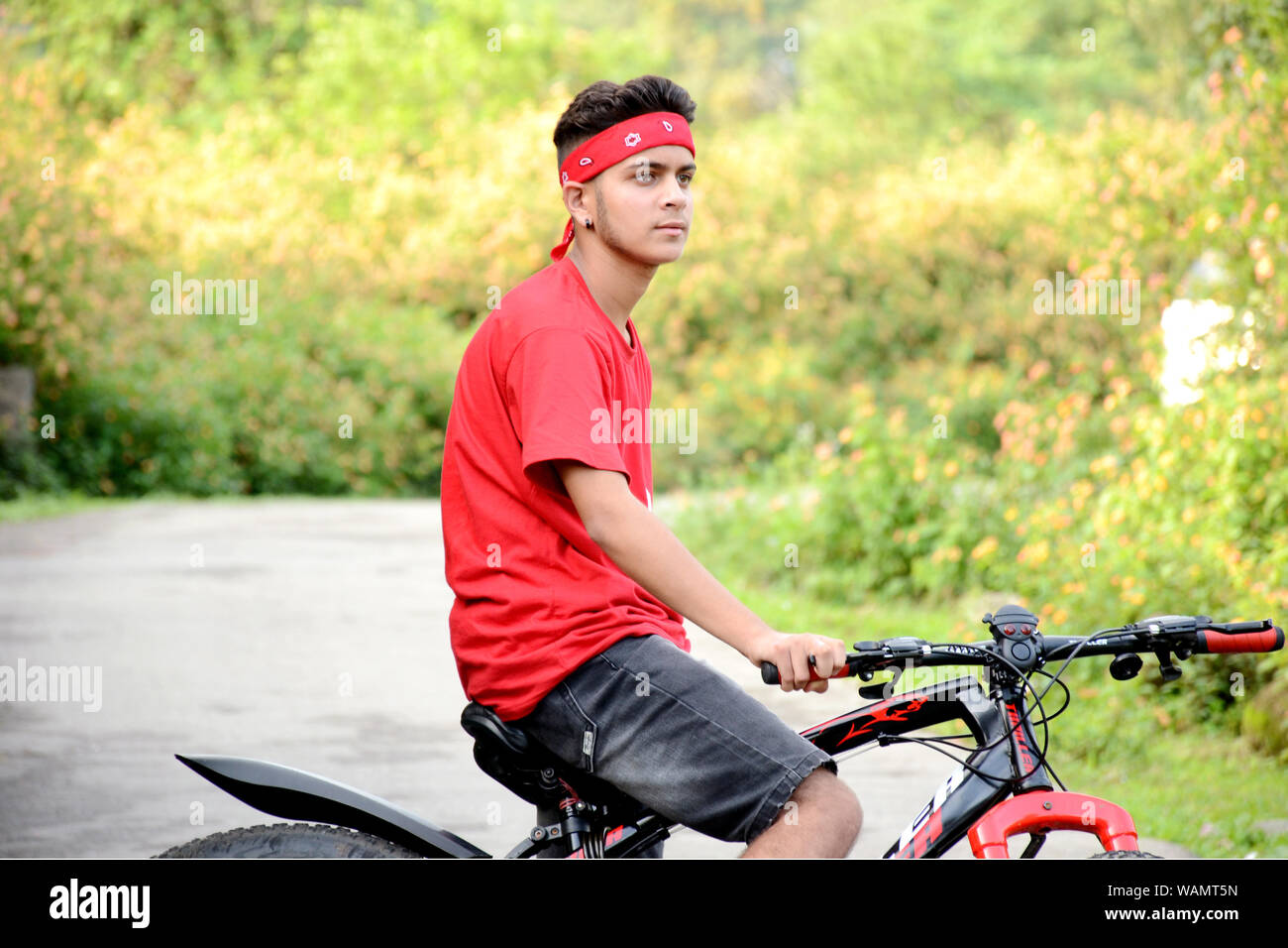 this photograph is good and boy sitting on cycle and natural moment the great style and carry the cycle this photograph background is blurr and green. Stock Photo
