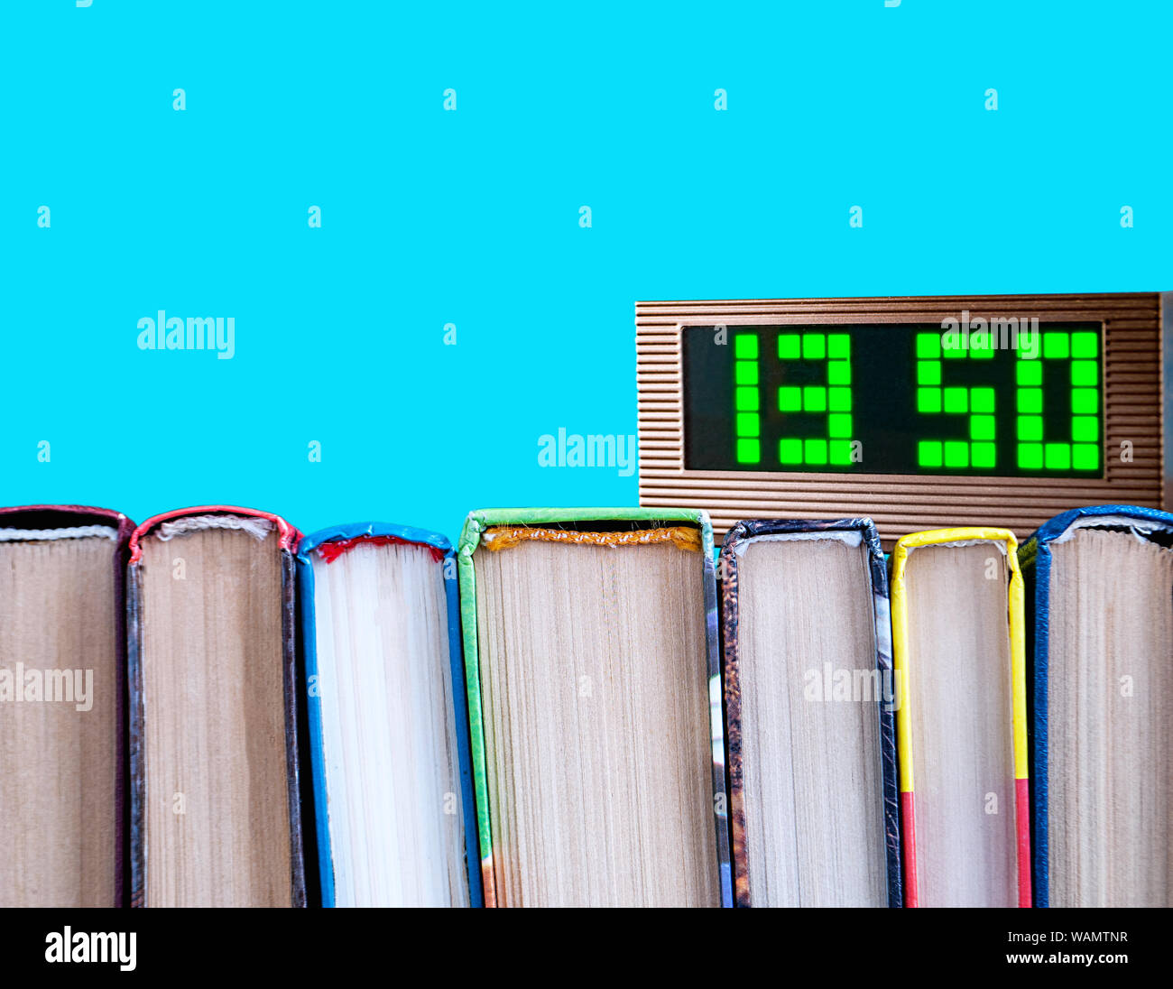 row of books and electronic clock on a blue background Stock Photo