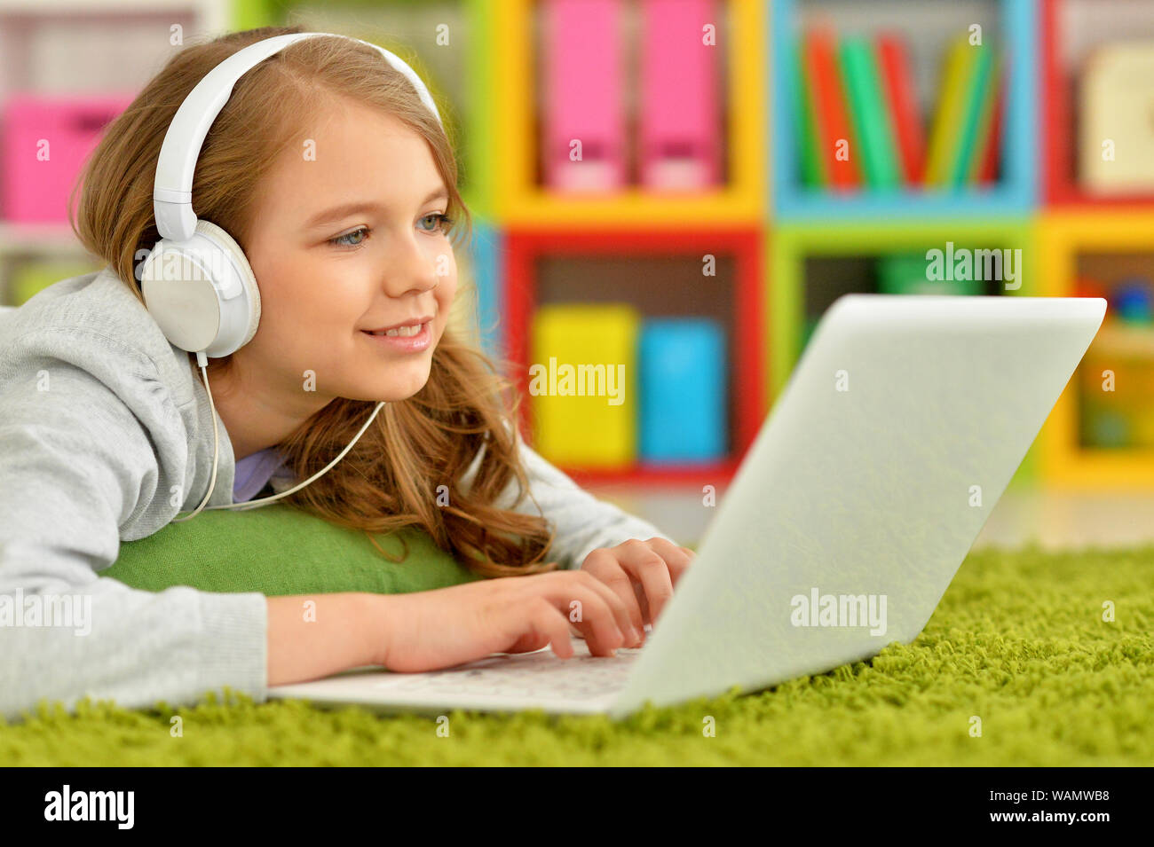 Emotional cute girl using laptop while lying on floor with green carpet ...