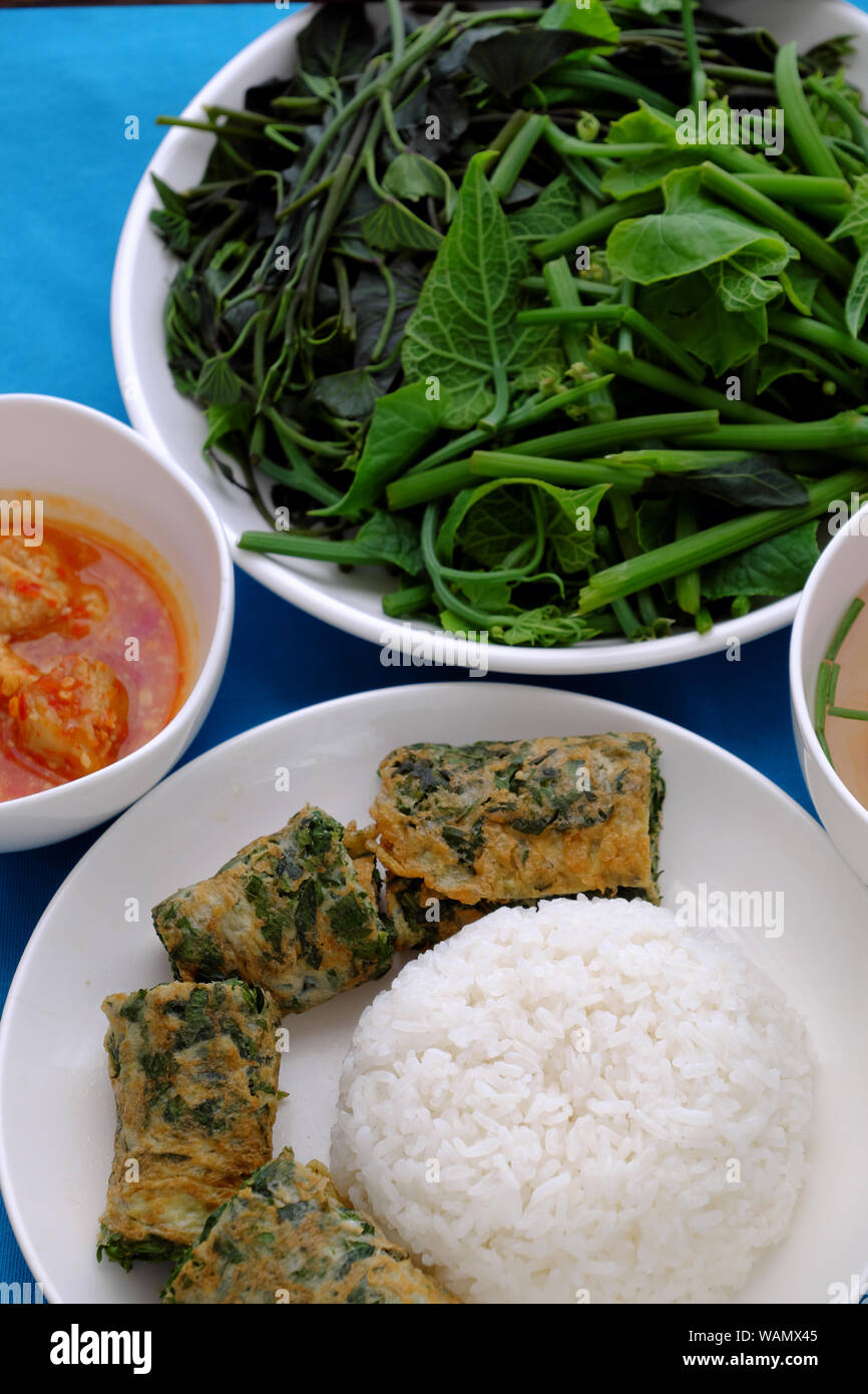 Top view Vietnamese meal lunch with boiled vegetables, tofu cheese, tomato soup, fried egg with mugwort, homemade vegan food for vegetarian on blue Stock Photo