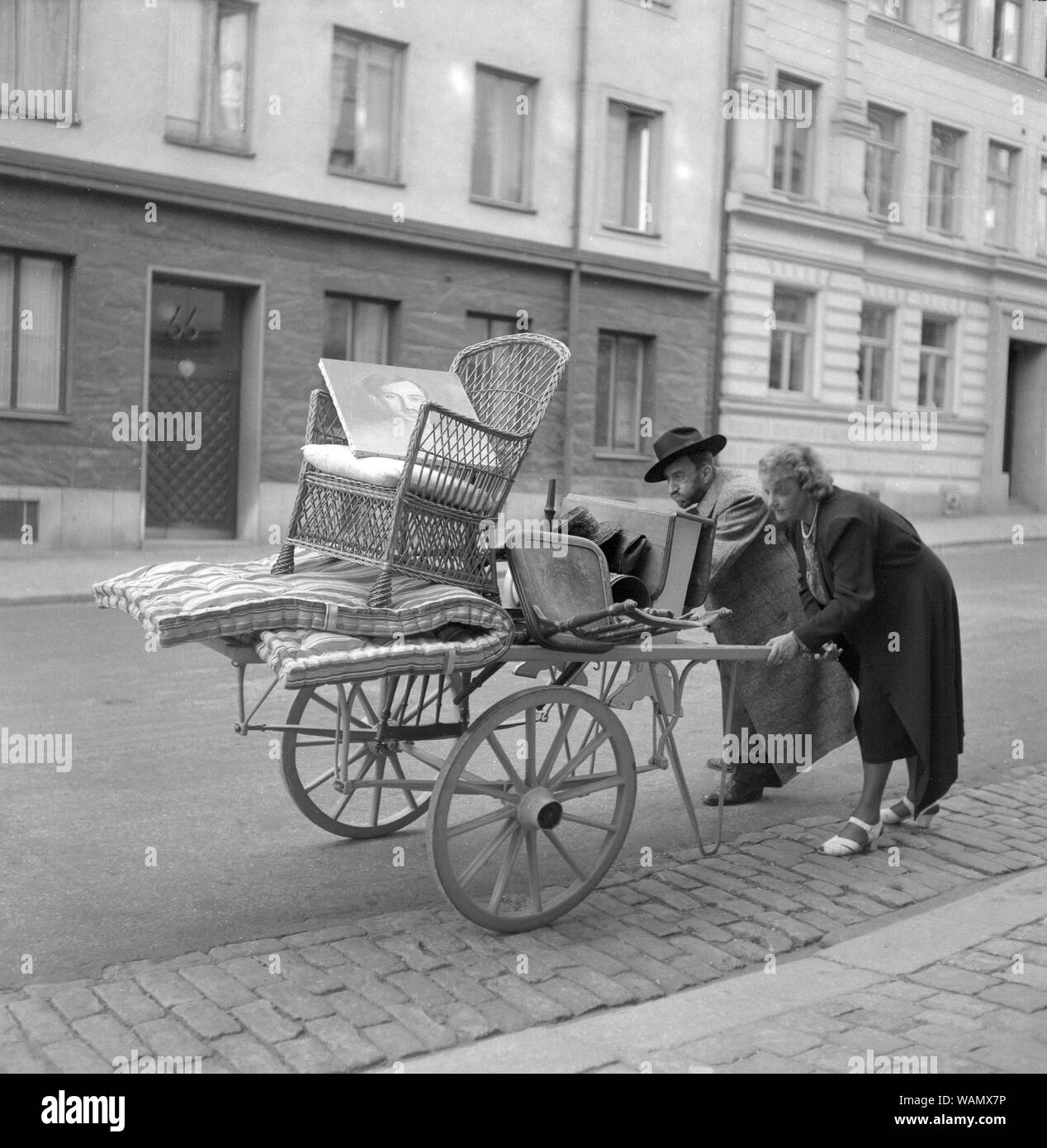 Moving in the 1940s. A couple are pushing a carriage in front of them with some furniture on it. They seem to struggle with it. Sweden 1943. Kristofferson ref C67-4 Stock Photo