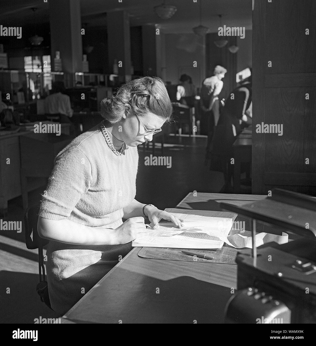 1950s office clerk.  A young woman is sitting at her desk and carefully examines the accounting and that the figures and numbers add up and is correct. Sweden 1950 Kristoffersson ref AY6-2 Stock Photo
