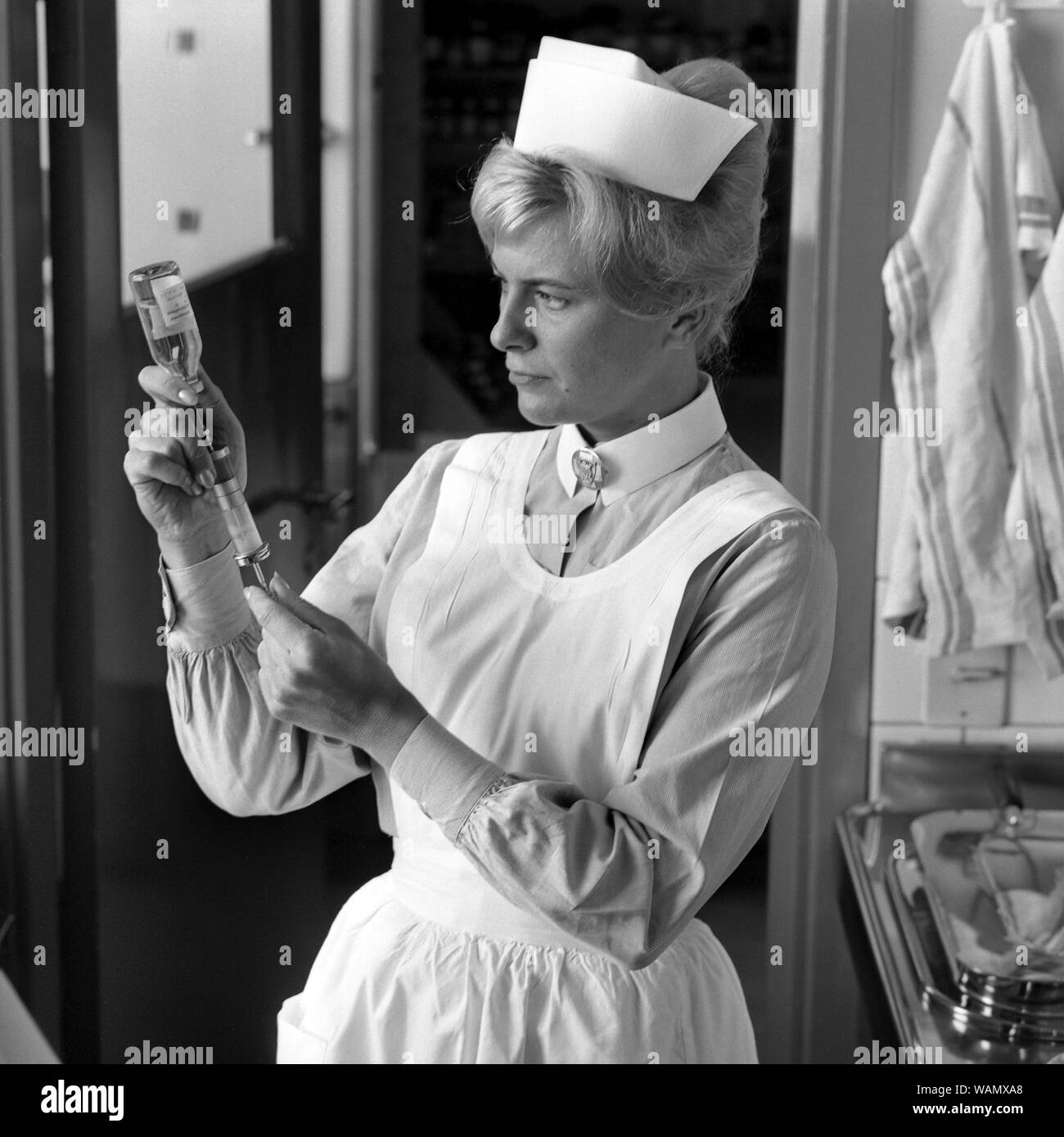 Nurse in the 1960s. A woman in a nurse uniform is preparing an injection and sucks the liquid from a bottle of medicine into a syringe. september 1963. Stock Photo
