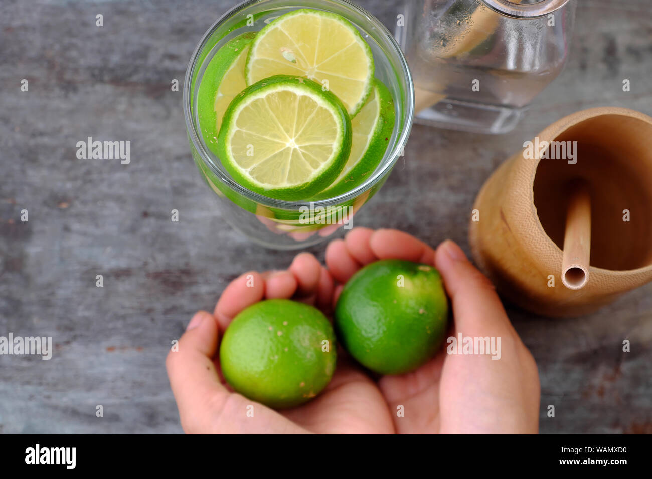 Close up woman hand hold lemons and lime slices for detox water on gray wooden background, a drinking water for healthy diet and skin care Stock Photo