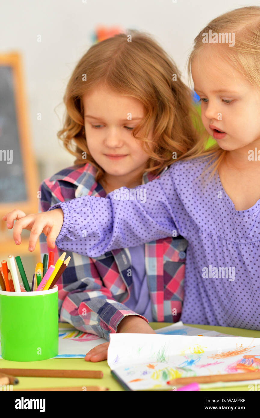 Cute little girls sitting at table and drawing with pencils in their ...