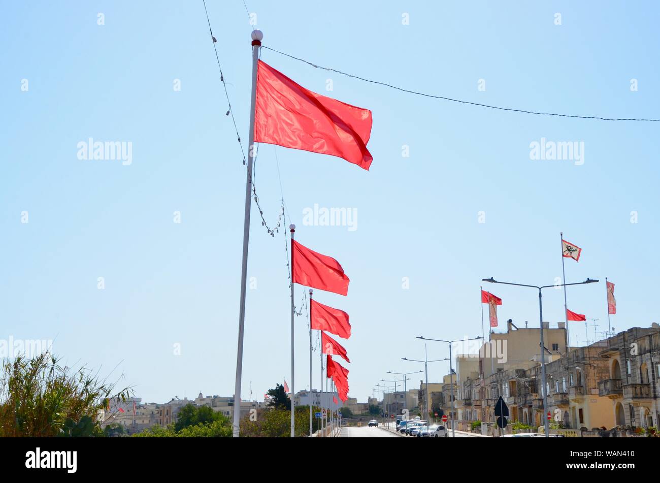 line of red flags flying from flagpoles in malta Stock Photo
