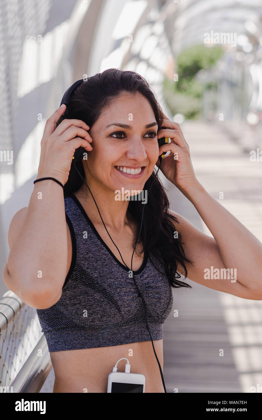 Young woman putting on headphones in the middle of a workout in the park Stock Photo