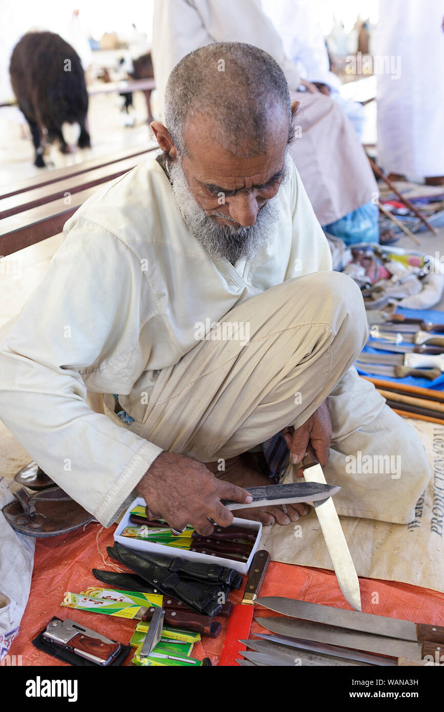 Man in traditional clothes selling knives, sharpening a knife at Sinaw market, Oman Stock Photo