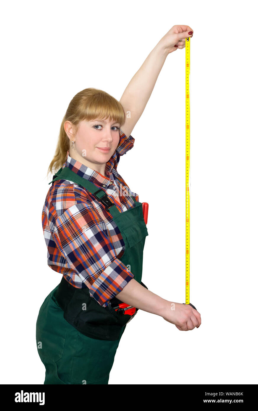 young woman in work overalls holding a tensioned tape measure isolated on white background Stock Photo