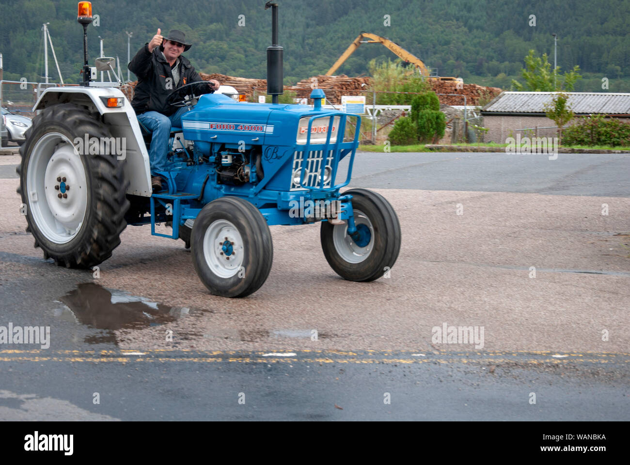 Man Stetson Hat Driving Blue White Ford 4000 Tractor male black jacket thumbs up gleaming front offside drivers side view Holy Loch Marina 1 pers Stock Photo