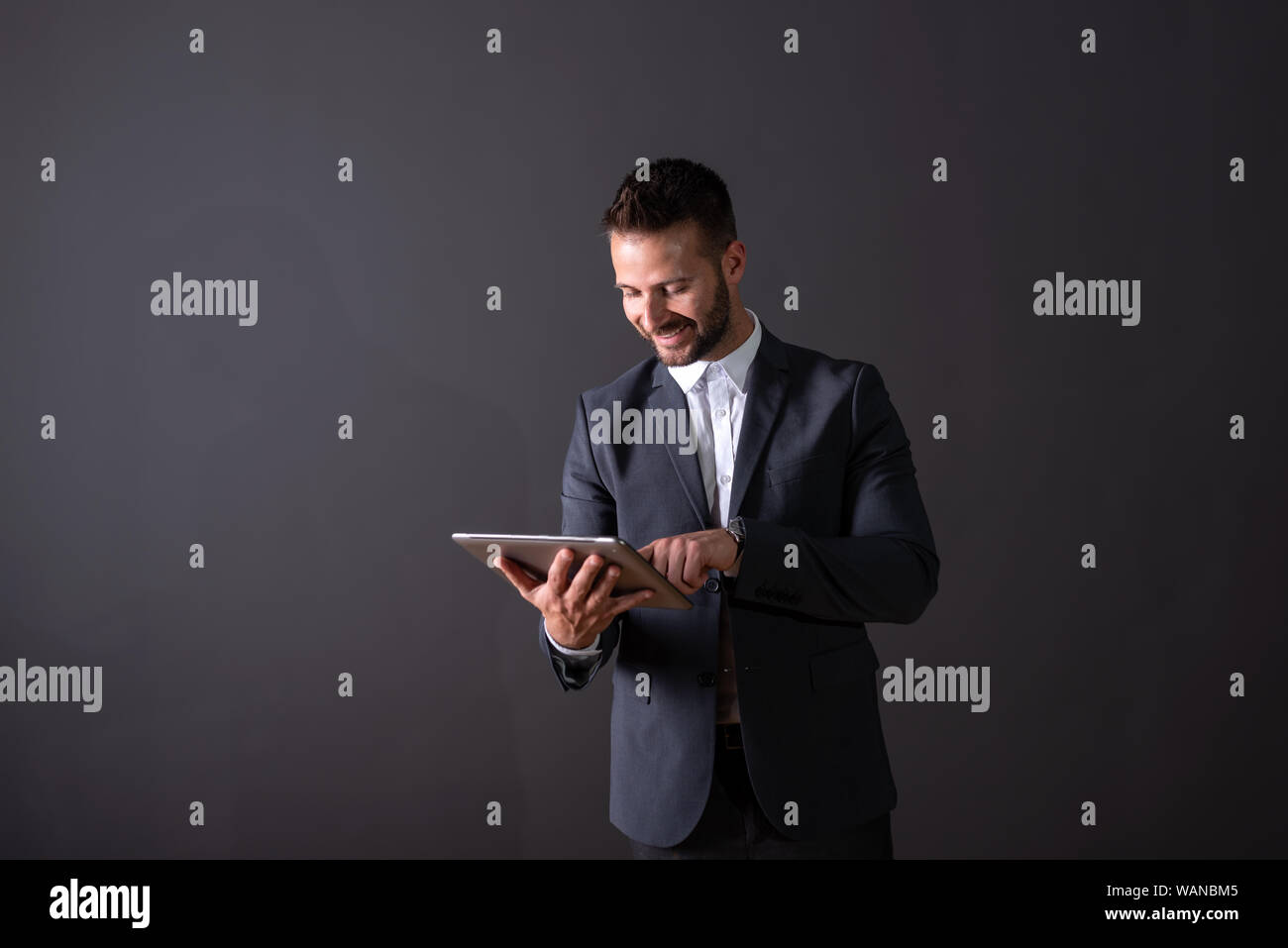 A smiling handsome young businessman in a suit using a tablet in front ...