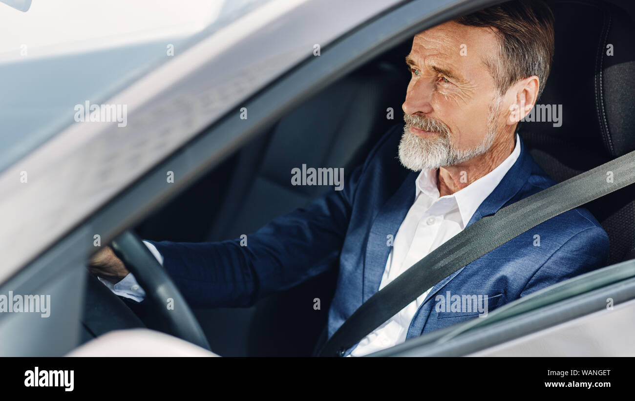 Side view of a mature businessman. Senior male concentrating on road while driving a car. Stock Photo