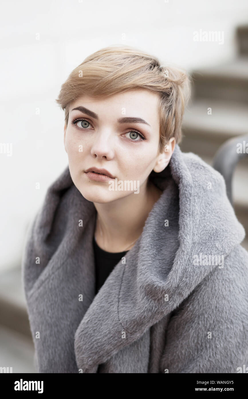 woman with short stylish hairstyle in gray coat on a white background Stock Photo