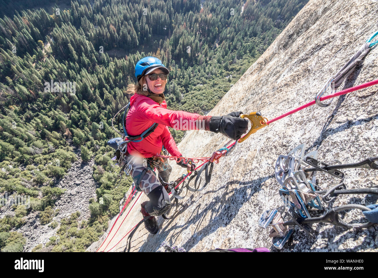 A young woman is all smiles while jumaring on a fixed rope way high up Stock Photo