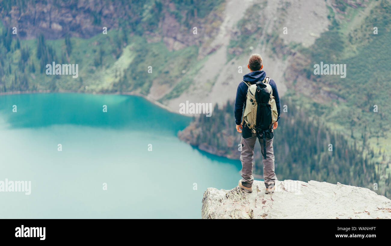 Male hiker is standing on a cliff looking at the lake in Glacier NP Stock Photo