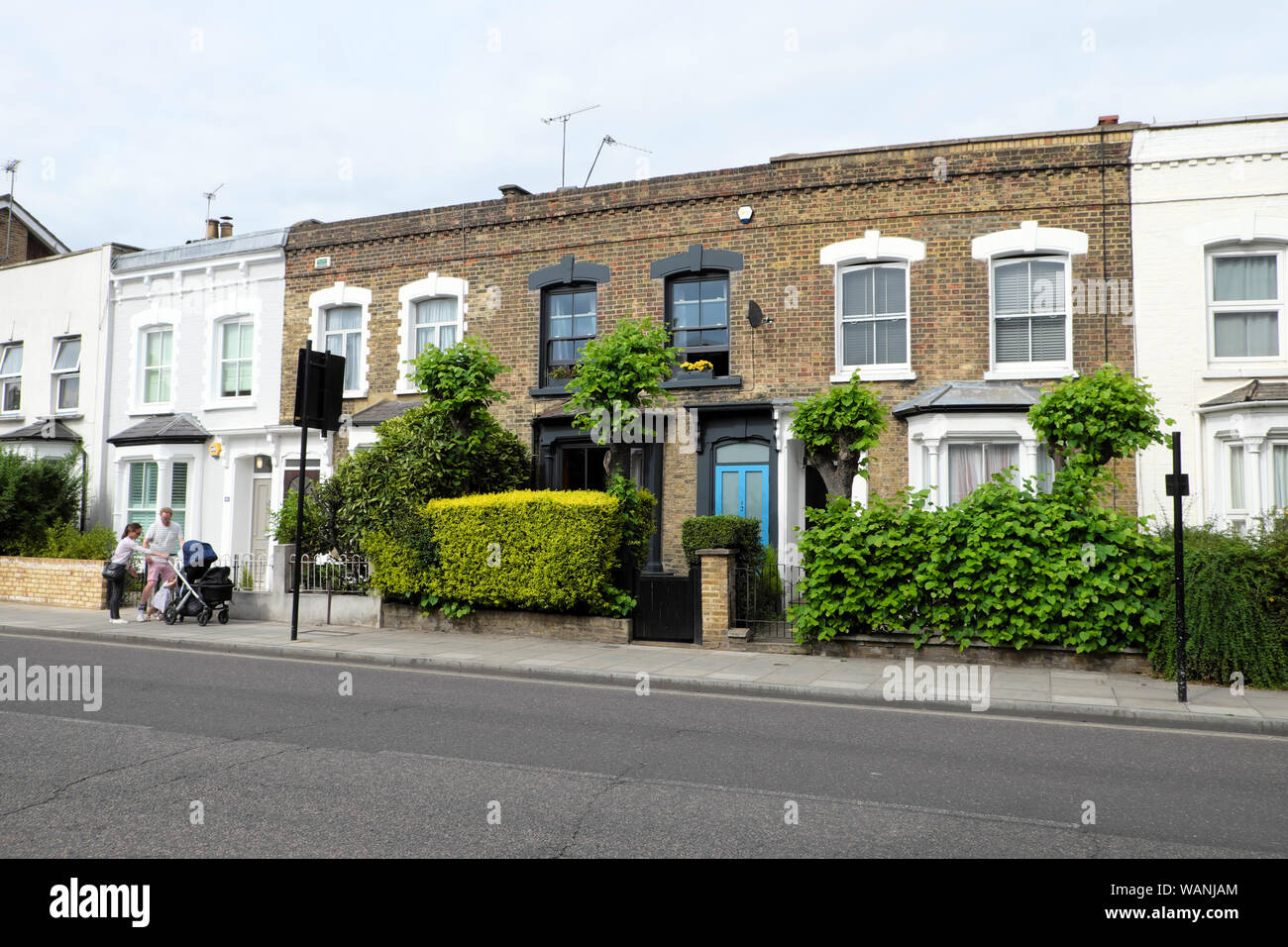 A young family with child and pushchair walking past a row of terraced houses on Green Lanes in Newington Green London N16 England UK  KATHY DEWITT Stock Photo