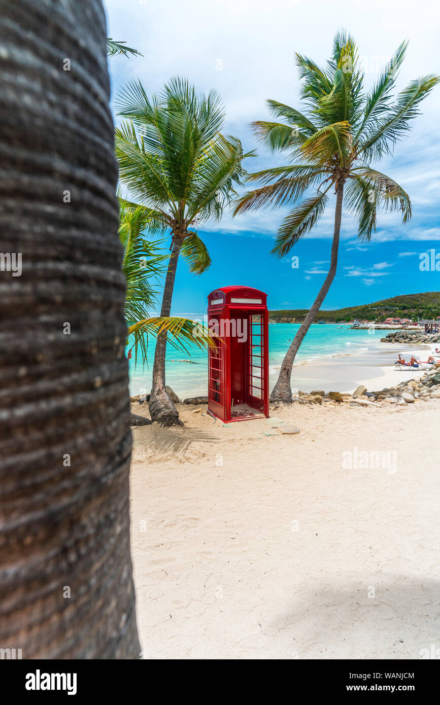 Red british phone box in front of the clear Caribbean Sea, Siboney Beach, Dickenson Bay, Antigua Stock Photo
