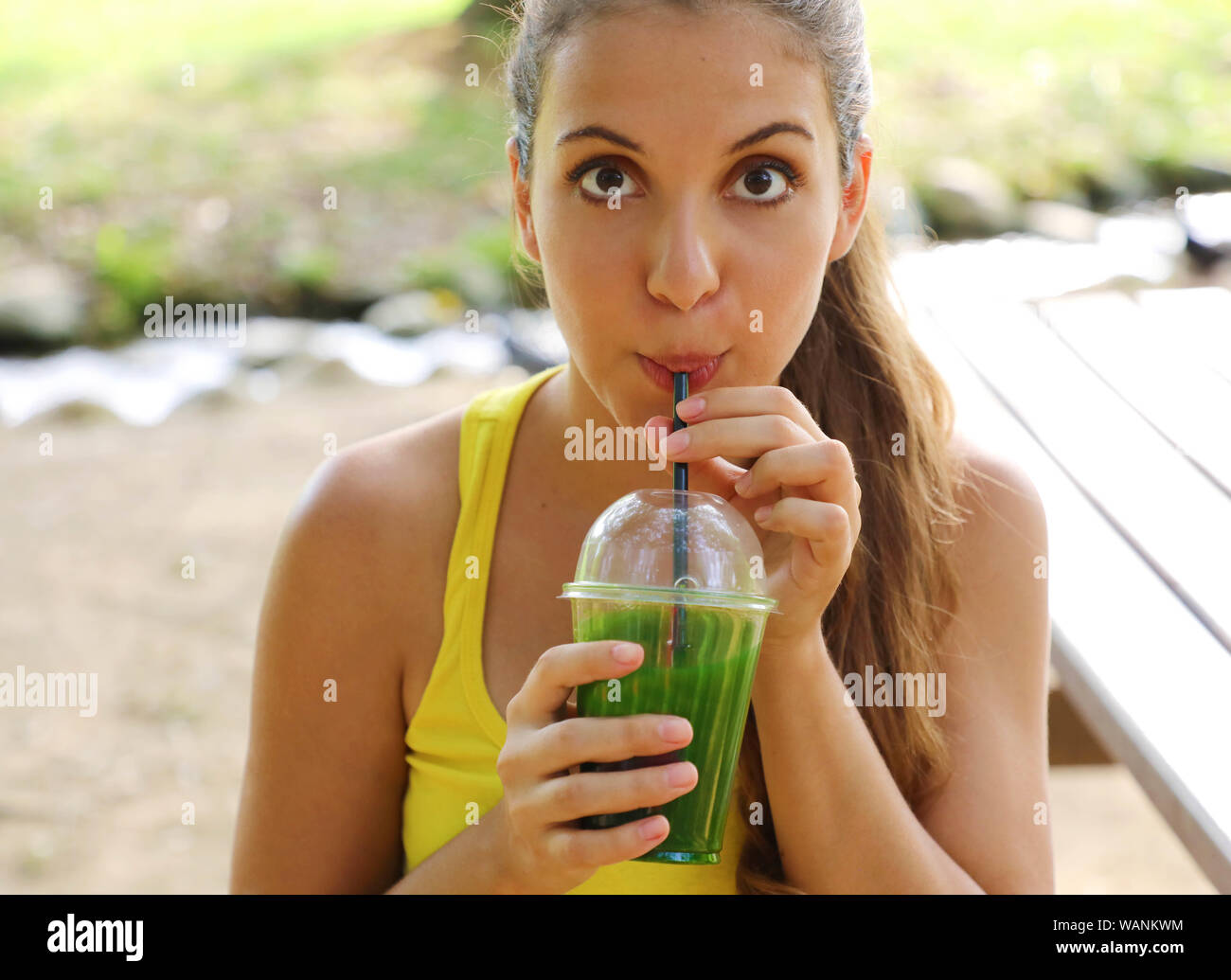 Close up of fitness girl looking at camera and drinking green detox juice in the park. Stock Photo