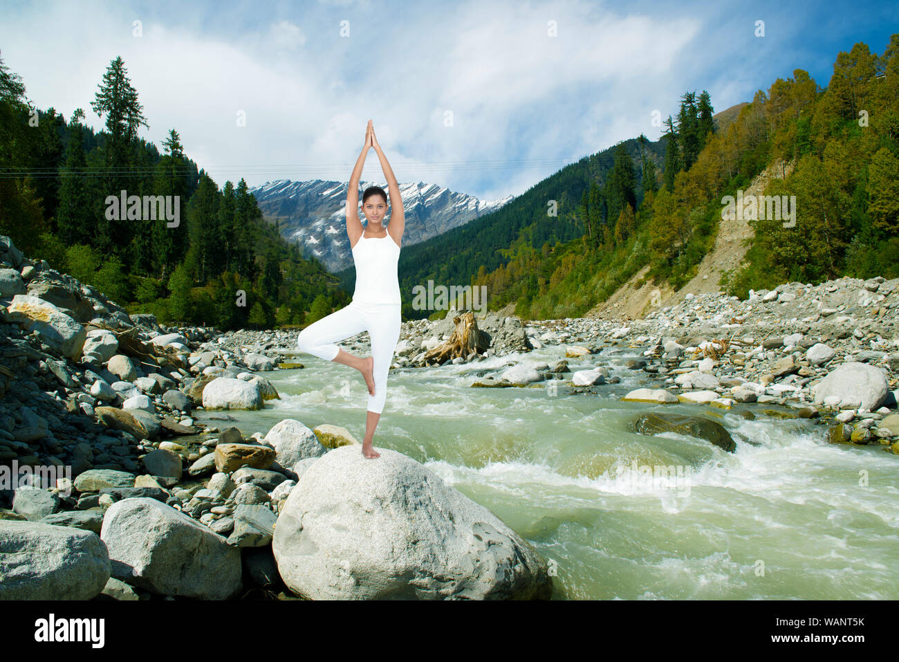 Young woman practicing yoga standing on a rock at riverbank, Beas River, Manali, Himachal Pradesh, India Stock Photo