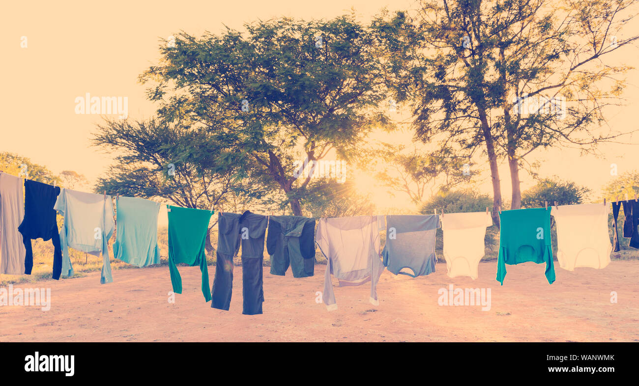 Mens and womens laundry drying on outdoor clothes line with pegs and sun streaming in behind with retro Instagram style filter effect Stock Photo