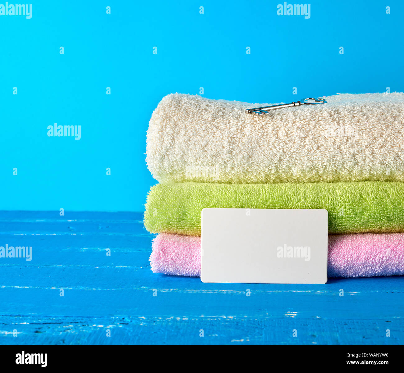 three multi-colored new terry bath towels folded on a blue wooden background and empty paper business cards Stock Photo