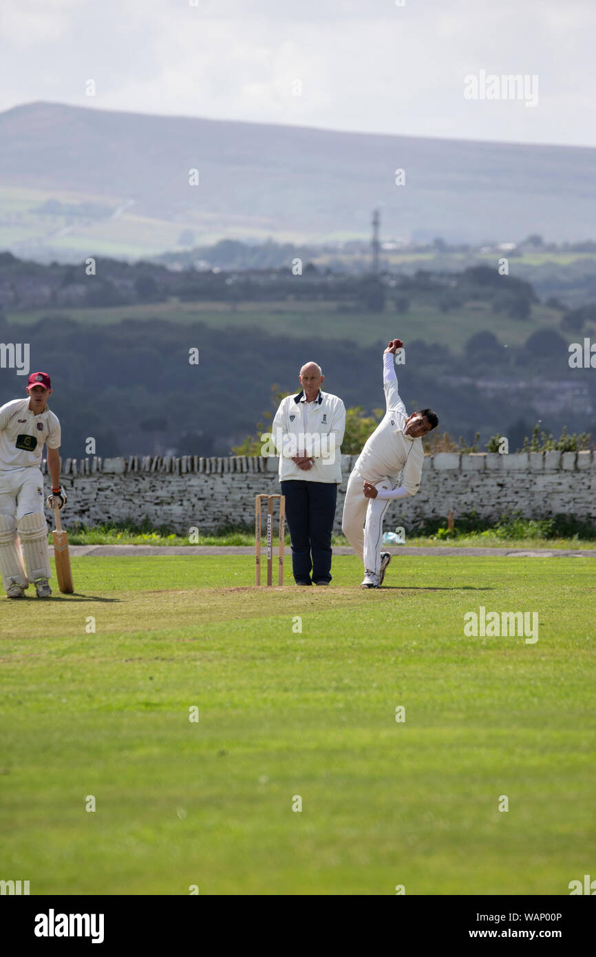 Cricket bowler in a village cricket match passing the umpire and about to deliver a ball at Kirkheaton in West Yorkshire, England Stock Photo