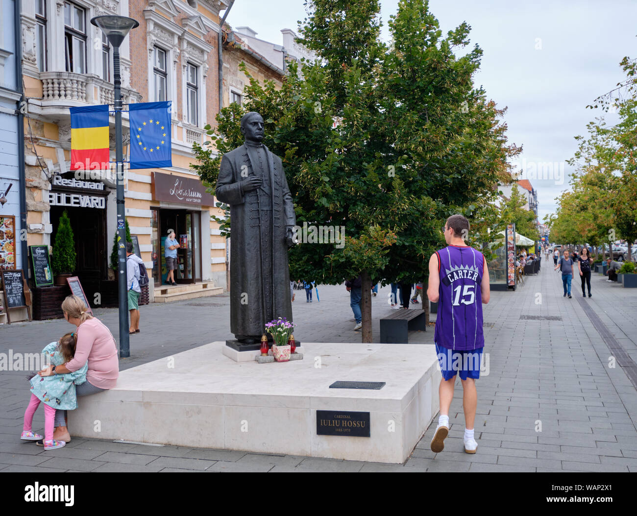 Tourist wearing a Raptors Carter no.15 Jersey walking by statue of cardial Ioliu Hossu in Cluj, Romania, August 17, 2019 Stock Photo