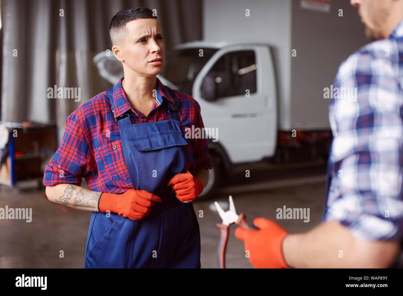 Female automechanic in the uniform listens to her mentor as he explains her what to do. Stock Photo