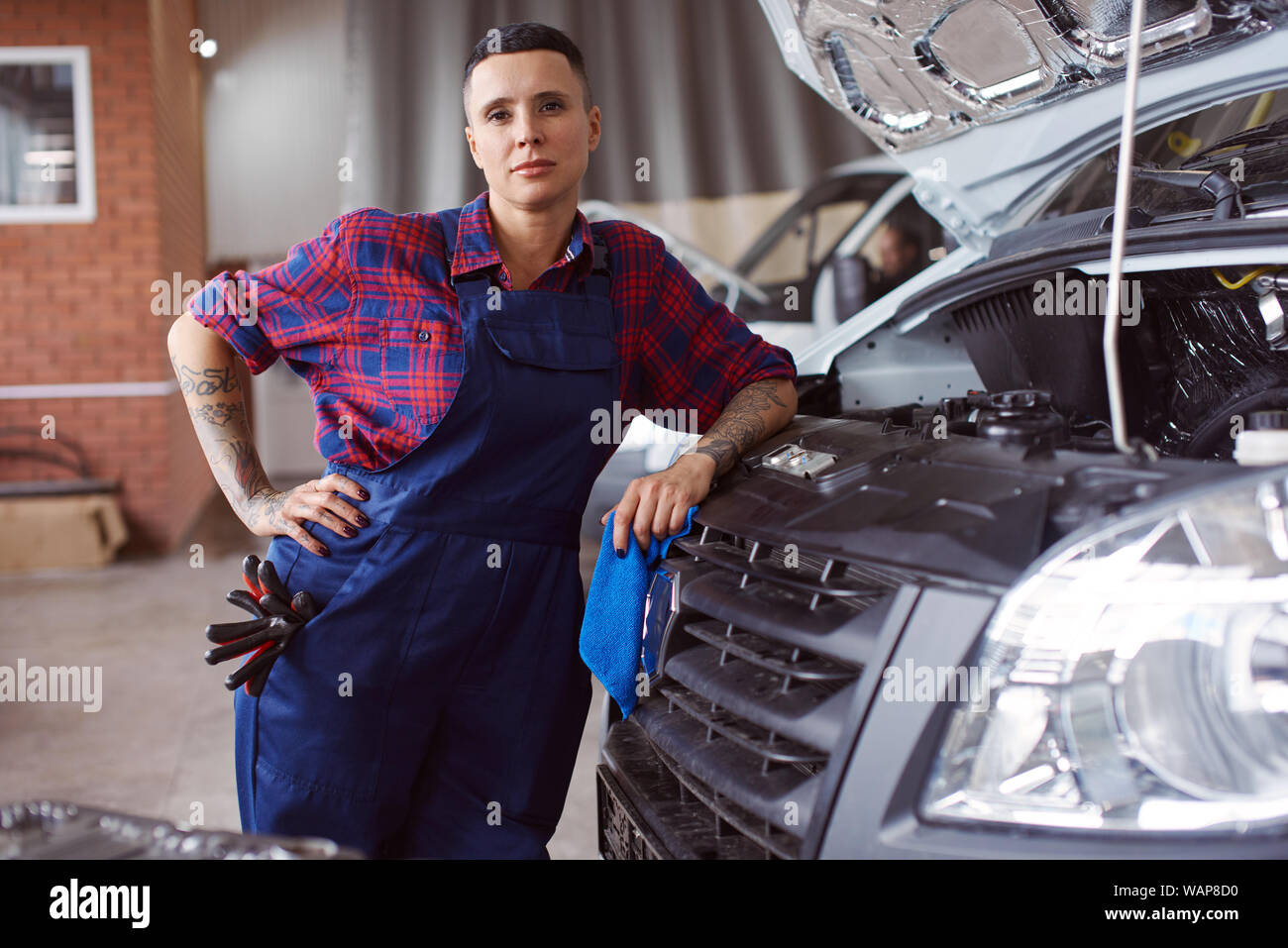 Vertical portrait of a woman automechanic standing next to a broken truck as she is cought in the middle of the working process. Stock Photo
