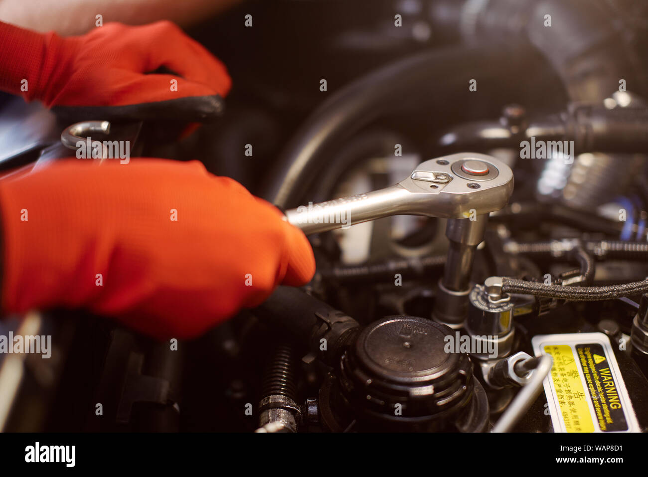 Close up of a car fixing process in the workshop where mechanic wears red gloves to protect himself. Stock Photo