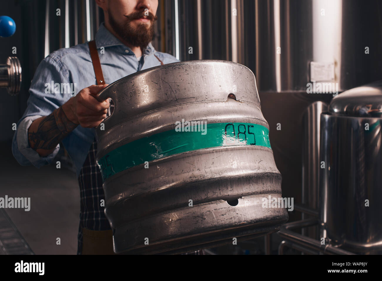 Brewery worker adds more beer to the bigger barrel from smaller one he holds and it looks like it is really difficult job to do. Stock Photo