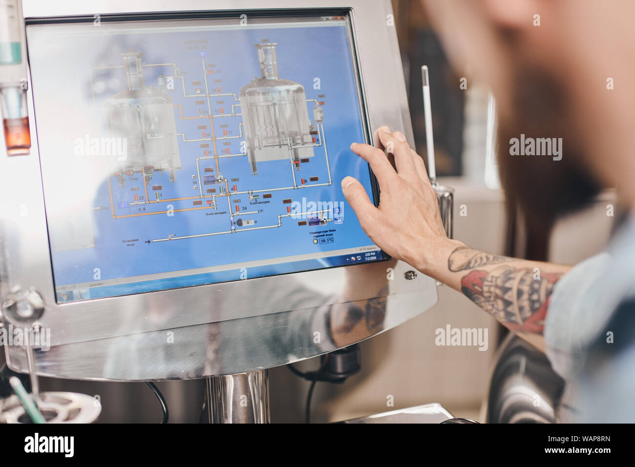 Brewery worker uses touch screens on the barrels to change storage settings. Stock Photo
