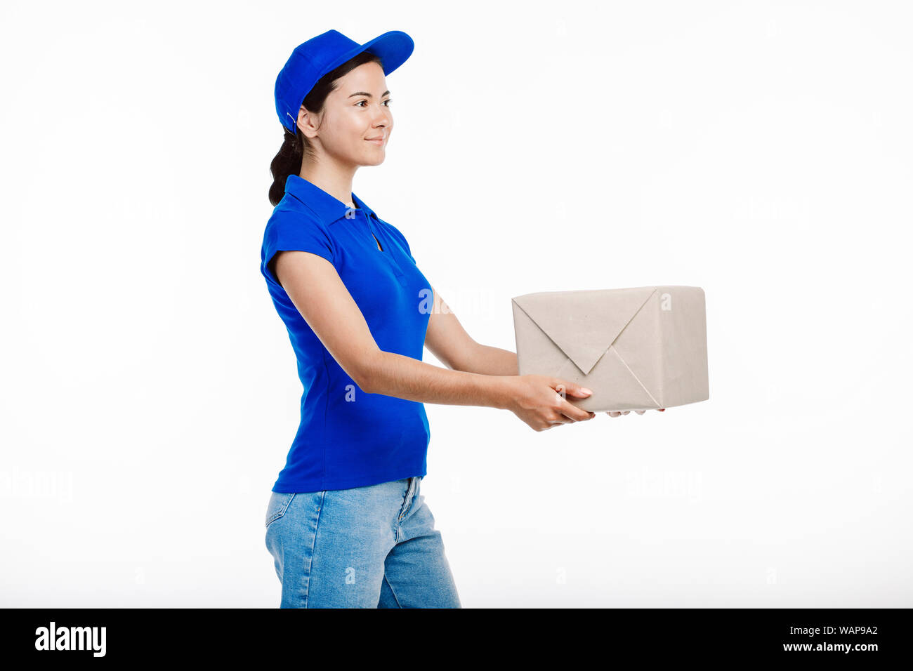 Deliery girl pictured while she gives the delivery to the client. She wears all blue uniform and smiles at someone. Stock Photo