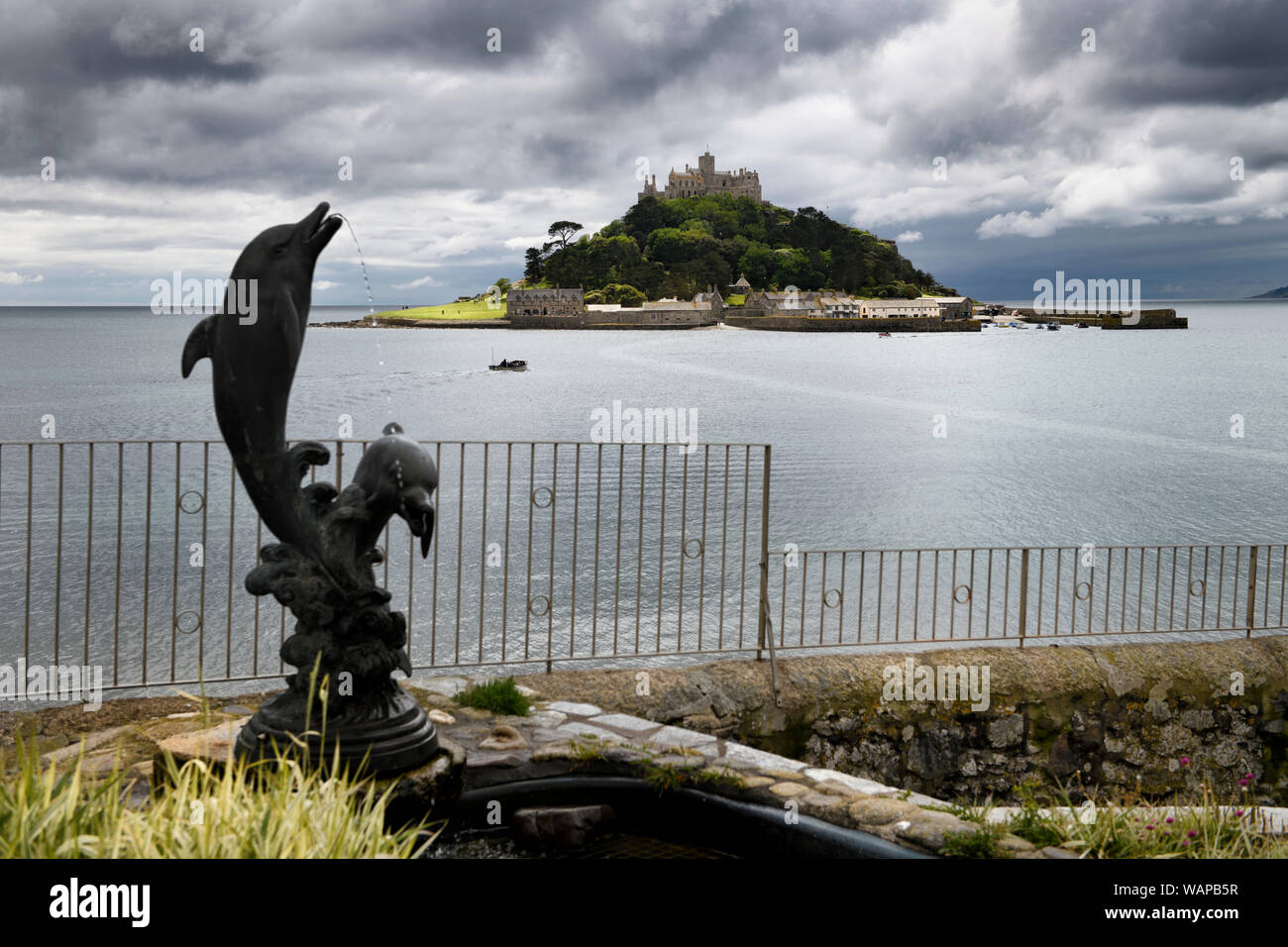 St Michael's Mount under cloudy skies with submerged walkway to Marazion from The Square with Two Dolphins sculpture Cornwall England Stock Photo